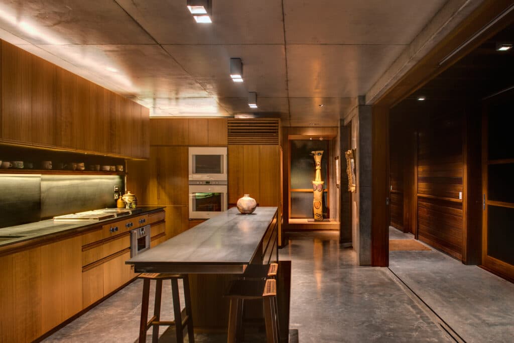 Modern kitchen with wooden cabinets, long island, pendant lights, and a decorative sculpture in an alcove.