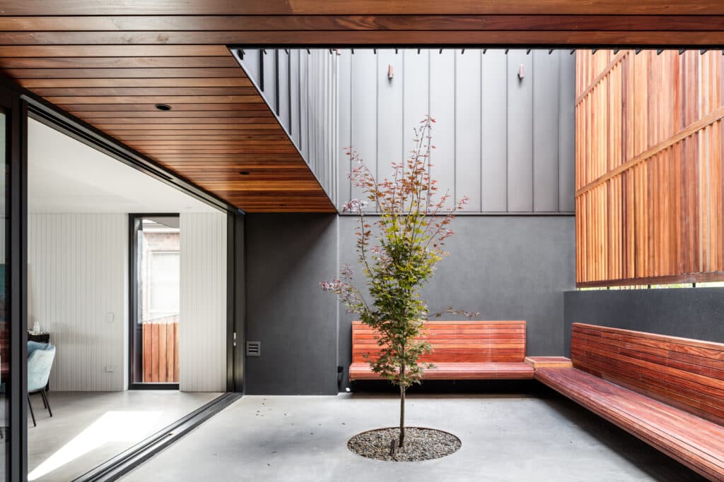 Modern courtyard with a central tree, wooden benches, and contrasting wood and metal paneling.