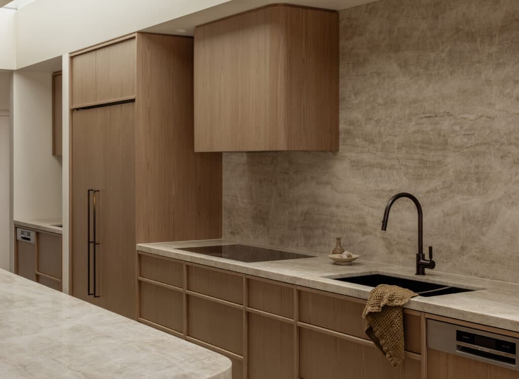 Modern kitchen with beige marble countertops, a sleek black faucet, wooden cabinets, and integrated appliances.