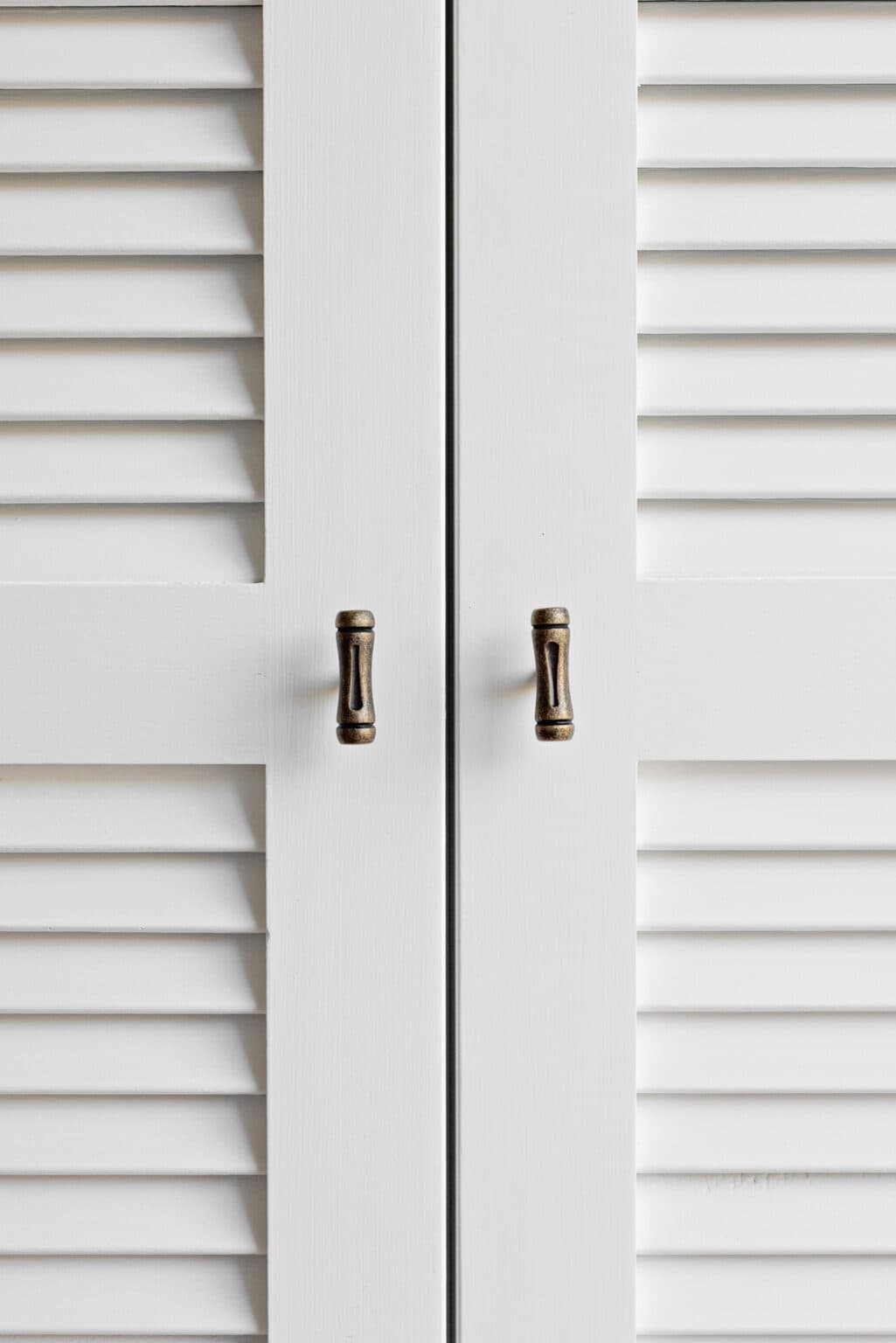 White louvered cabinet doors with two bronze handles in the center.