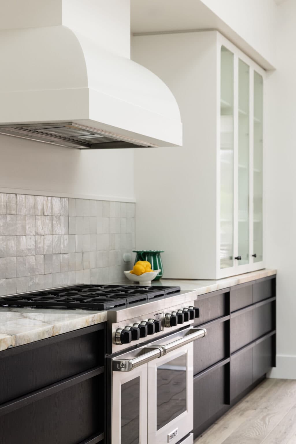 Modern kitchen with black cabinets, stainless steel oven, and a tiled backsplash. Lemons in a bowl add a pop of color.