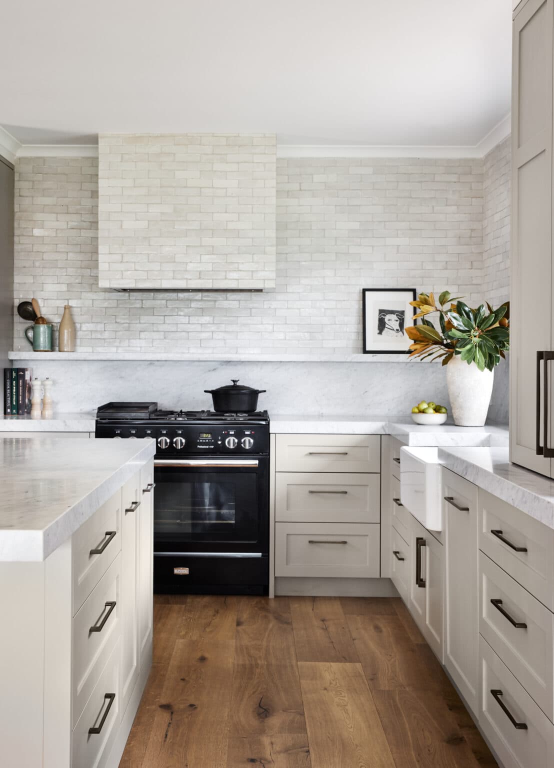 Modern kitchen with white cabinets, marble countertops, black stove, wood floor, and plant on corner counter.