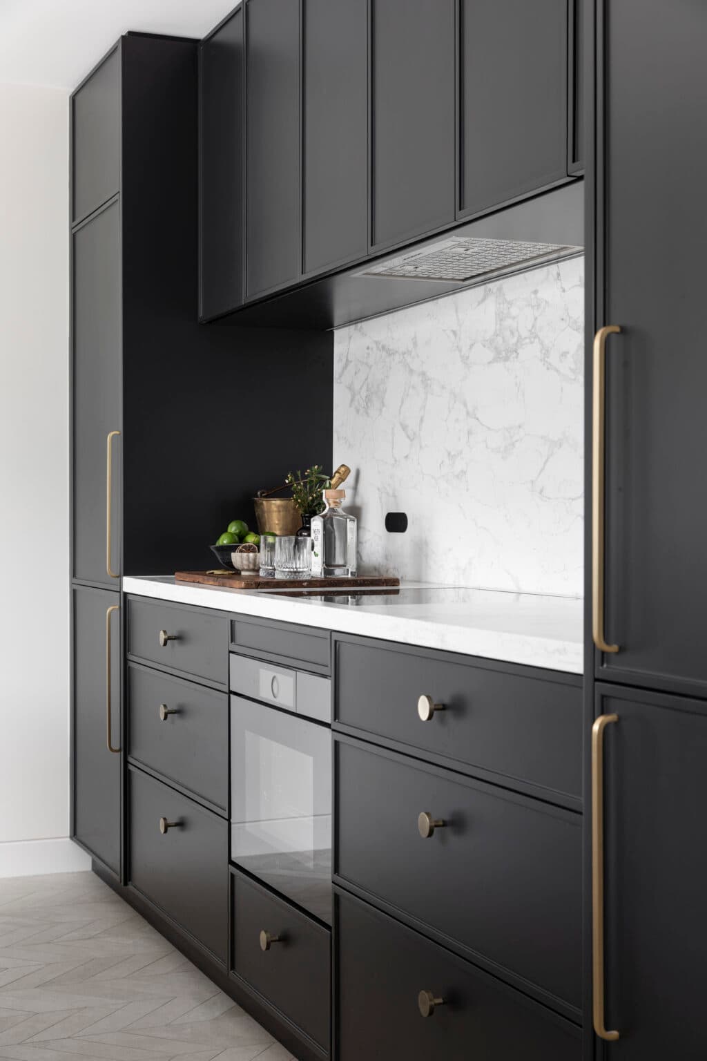 Sleek black kitchen cabinets, marble backsplash, and countertop; brass handles; cutting board with drinks and limes.