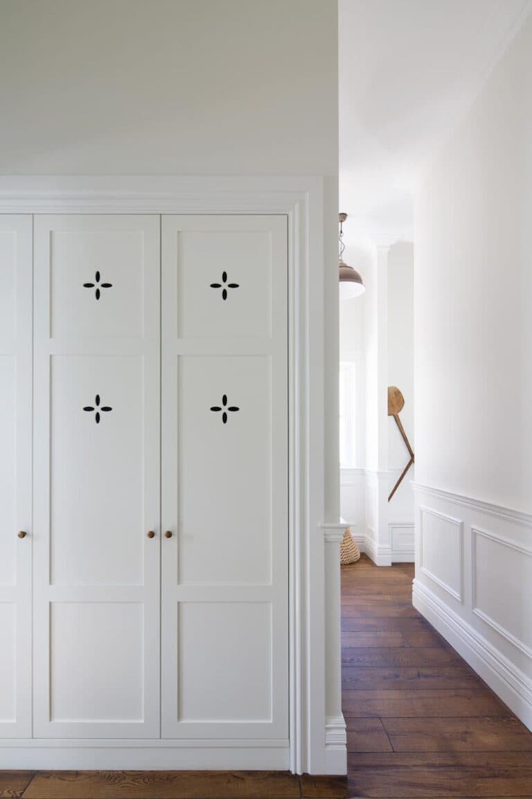 White closet doors with decorative cutouts next to a hallway featuring wood floors and white paneled walls.