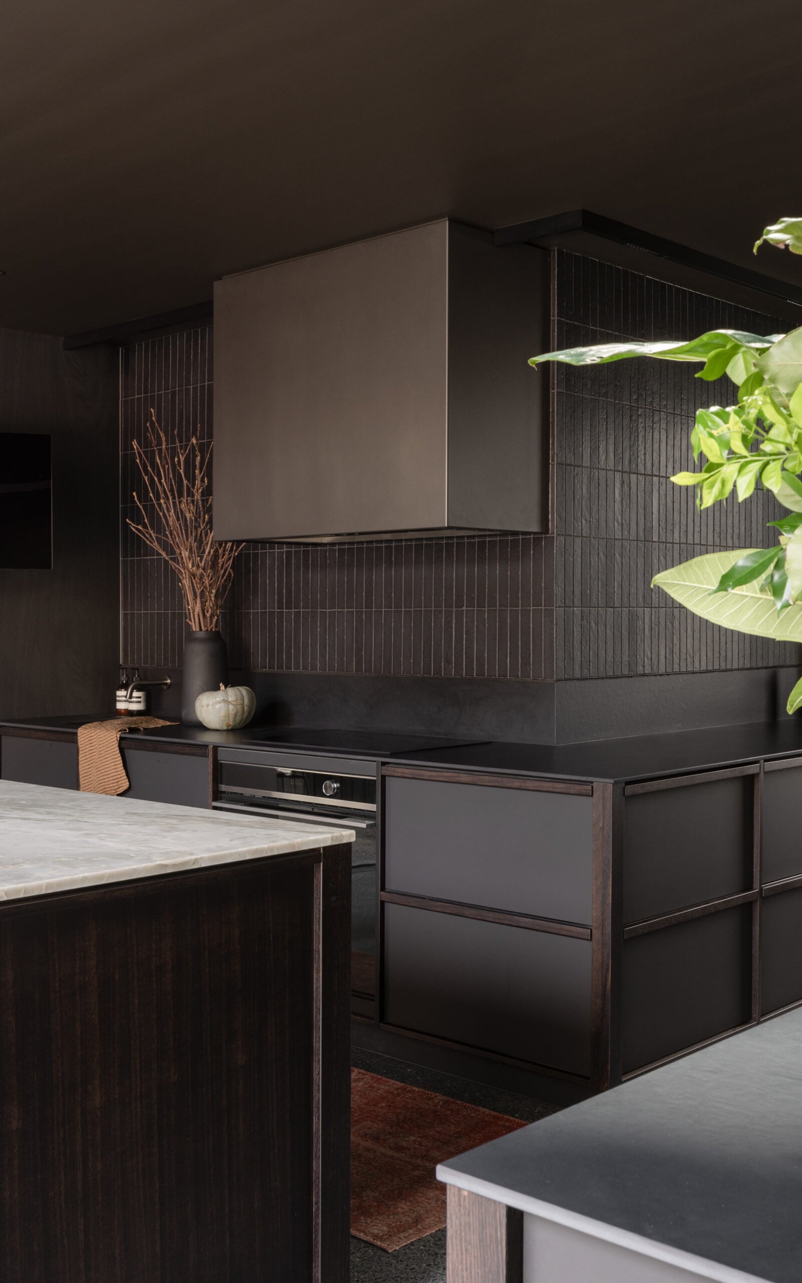 Modern dark kitchen with sleek cabinets, marble island, black backsplash, a vase with branches, and a small pumpkin.