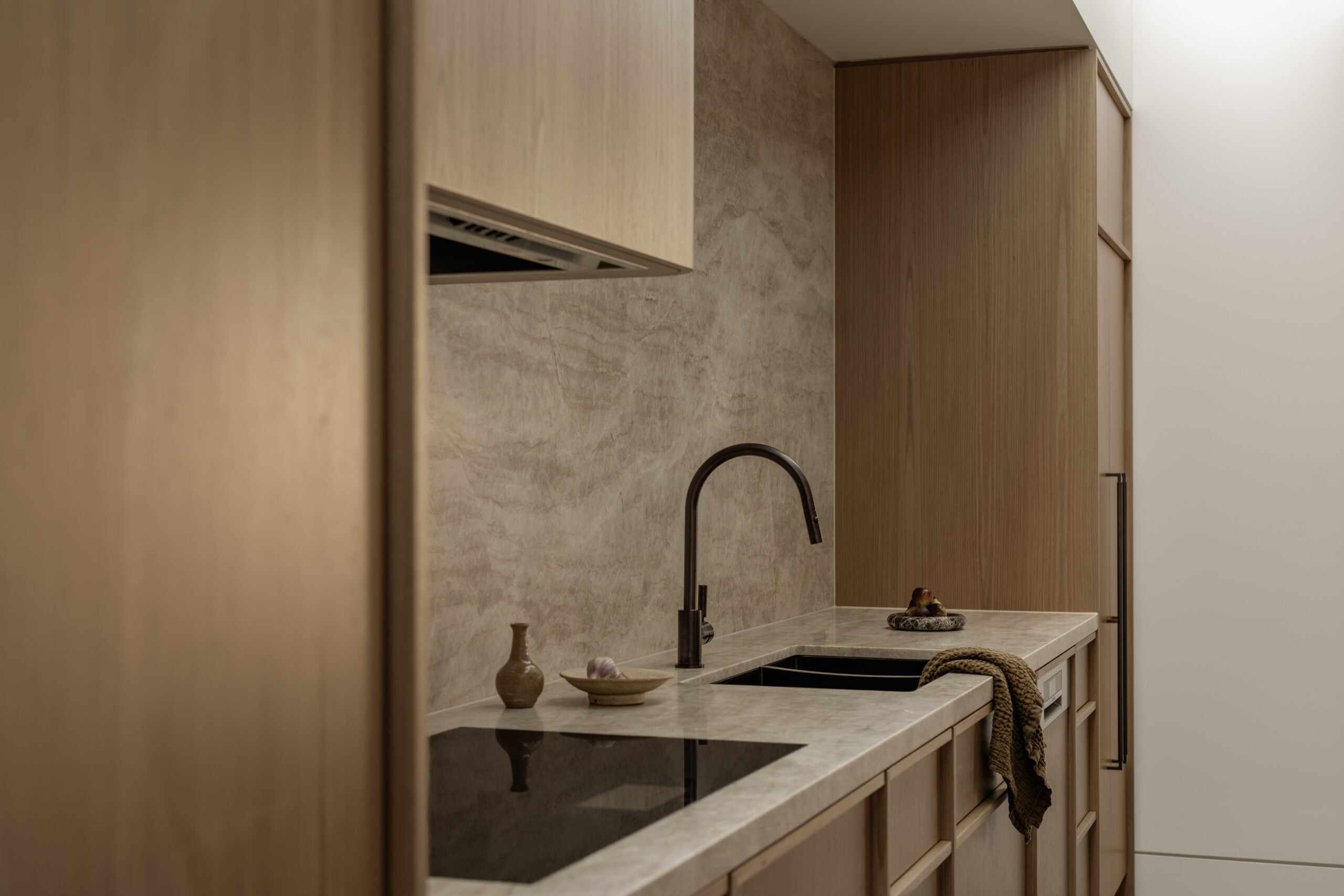 Modern kitchen with sleek marble countertops, minimalist wooden cabinets, an electric cooktop, and a black faucet.
